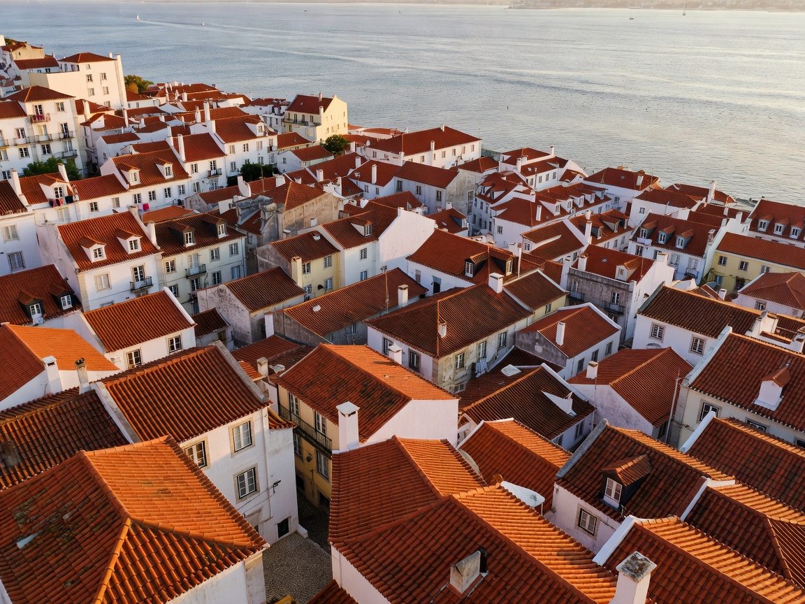 Terracotta rooftops of Lisbon sloping downward toward the broad Tagus River
